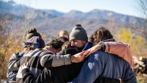 A group of friends embrace in a warm hug outdoors with a scenic mountain view.