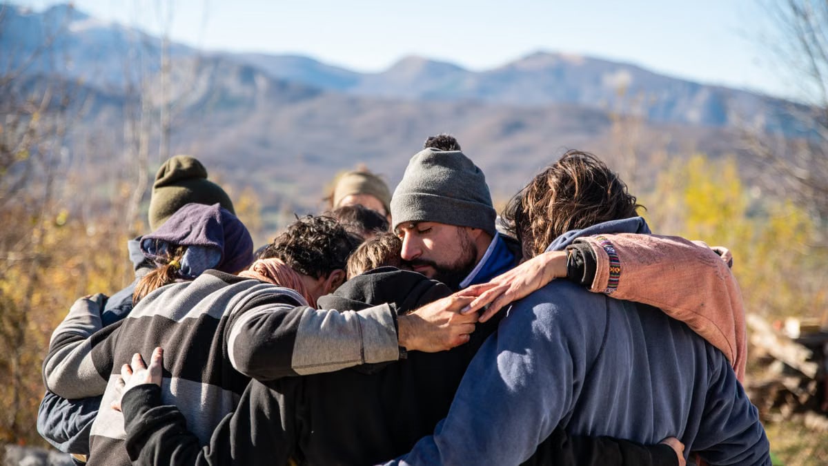 A group of friends embrace in a warm hug outdoors with a scenic mountain view.